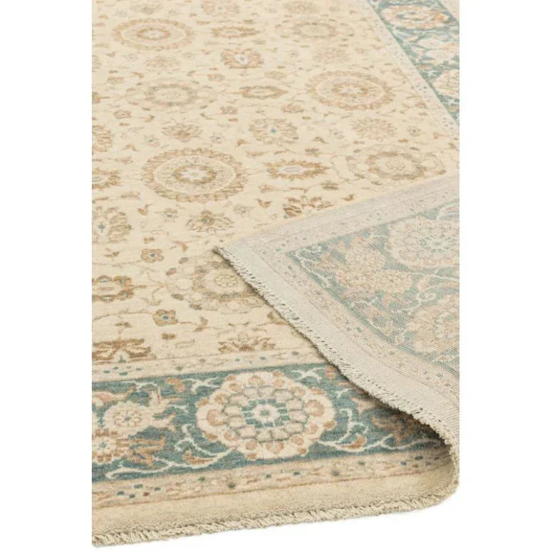 Cream patterned rug with teal and beige border, corner lifted to show underside detail