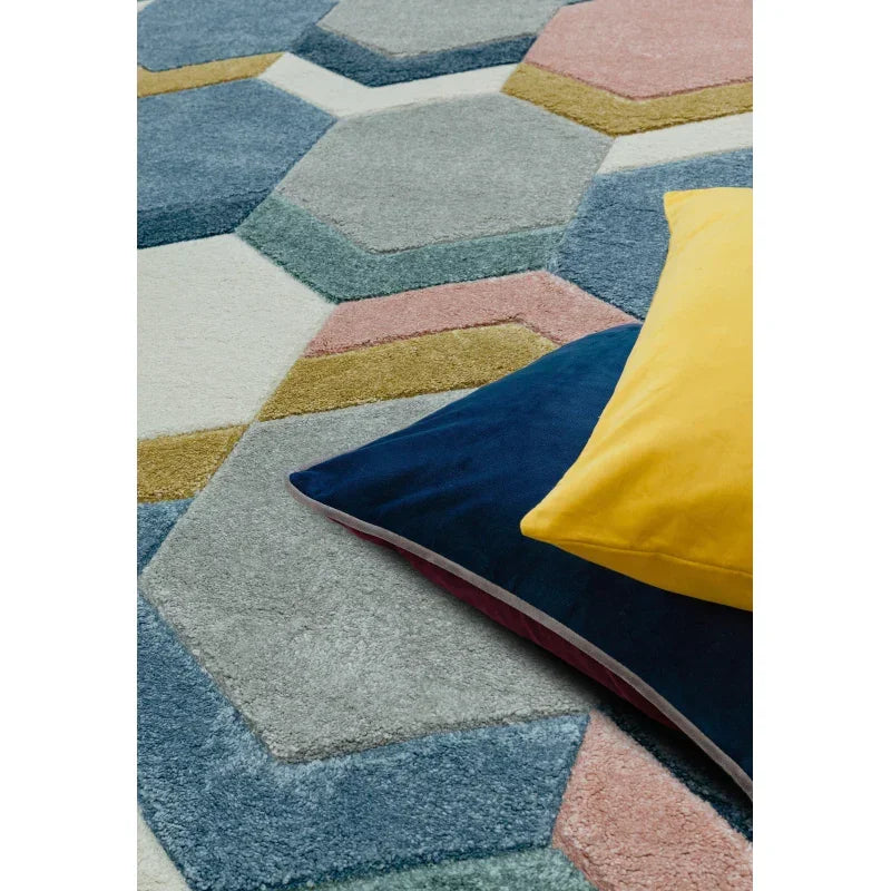 Geometric pattern rug in pastel colors with blue and yellow velvet cushions on top