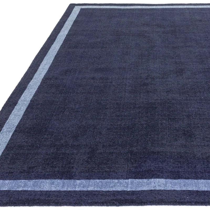 Navy blue area rug with a lighter blue border, viewed from corner angle