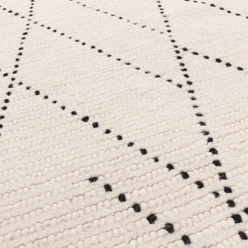 Cream wool rug with black diamond pattern and textured surface, close-up angle