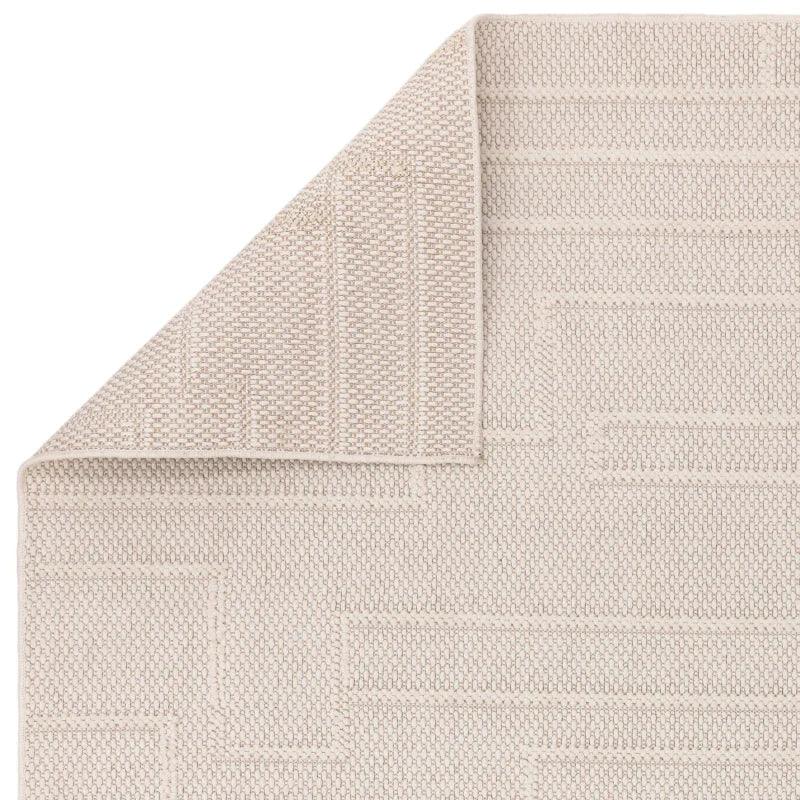 Beige textured area rug with geometric woven pattern and corner folded to show thickness