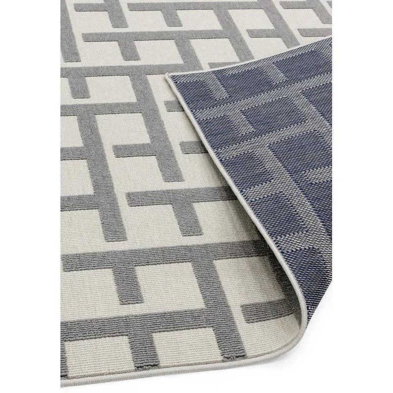 Geometric patterned area rug in grey and cream with corner flipped to show blue reverse
