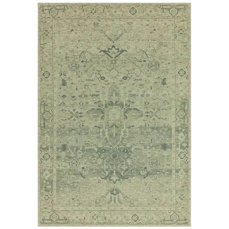 Green vintage area rug with faded floral pattern and distressed border design