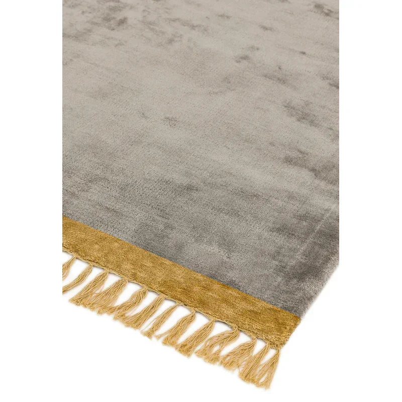 Grey area rug with gold fringe border and tassels, close angle of carpet texture