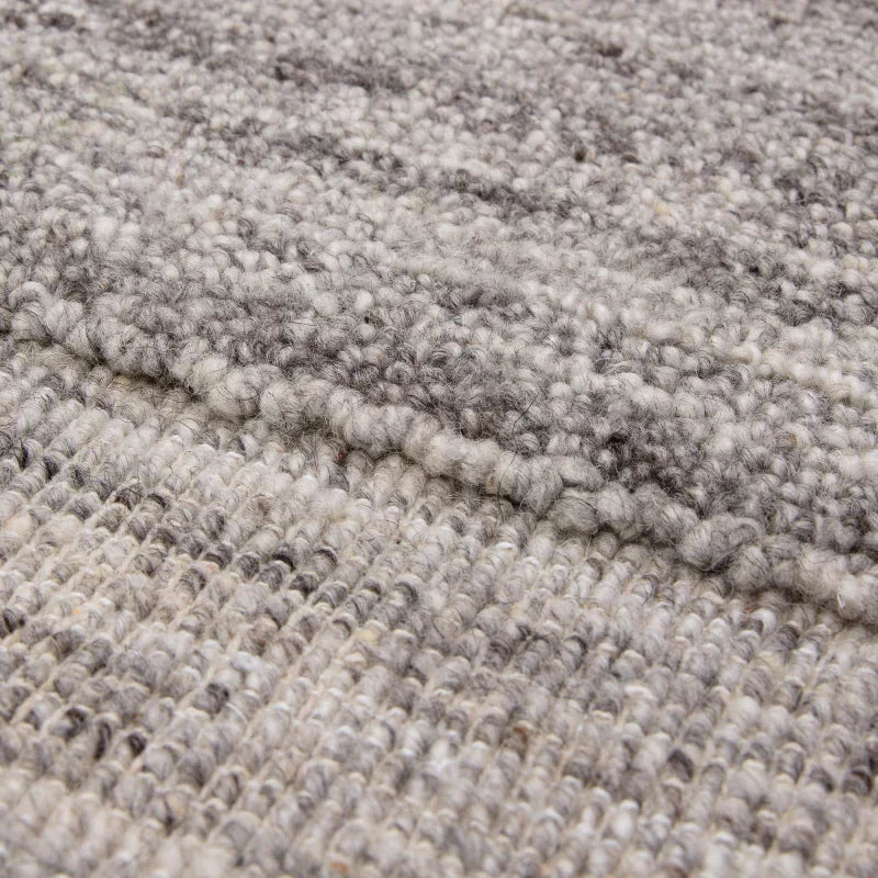 Closeup of textured wool rug in grey and cream tones showing woven pattern detail