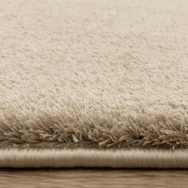 Close-up of beige plush carpet pile on wooden floor