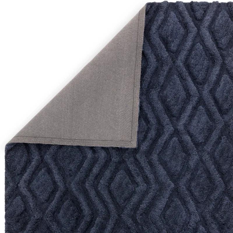 Dark blue geometric pattern rug with grey fabric backing, corner flipped up