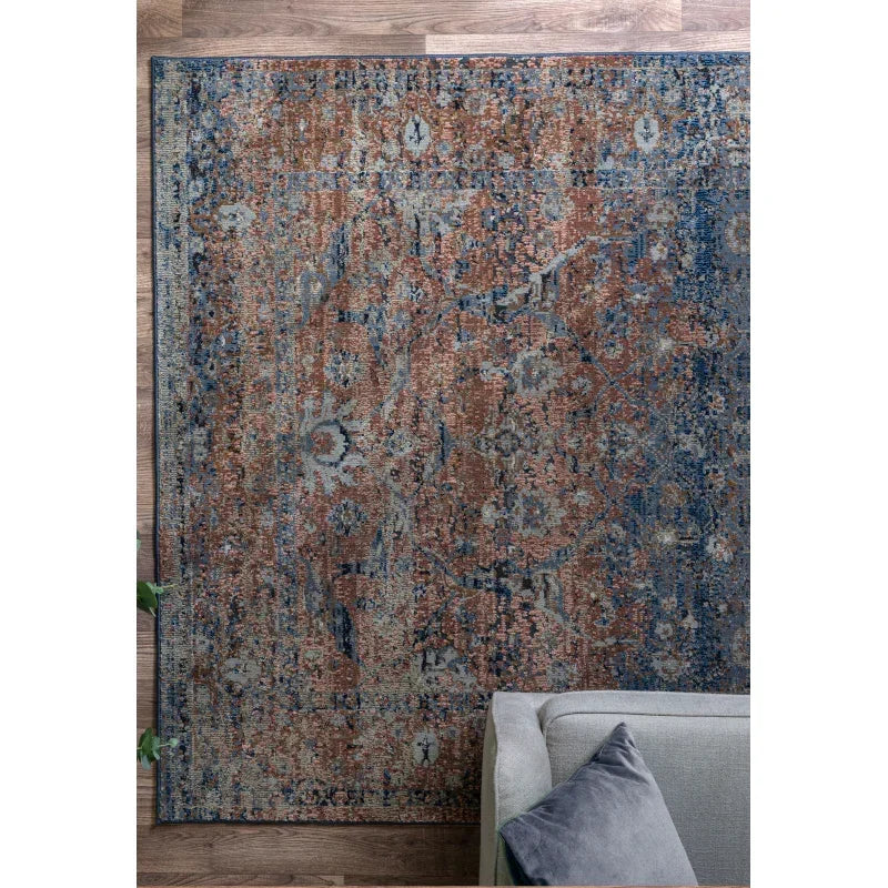Patterned area rug with blue and rust tones beside grey sofa on wooden floor