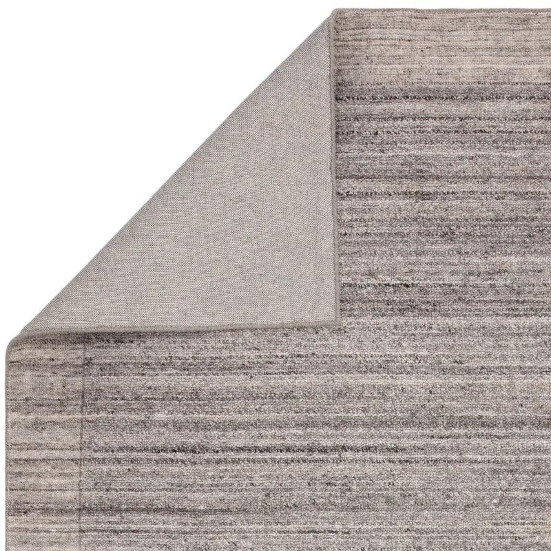 Grey textured area rug with corner folded to show backing