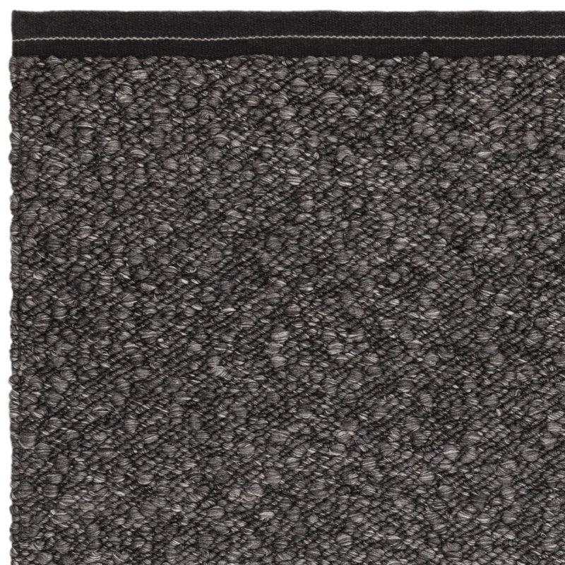 Close-up of grey textured loop pile carpet corner with stitched black border