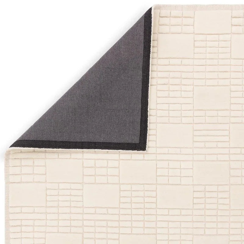 Cream geometric patterned rug with corner flipped showing black backing