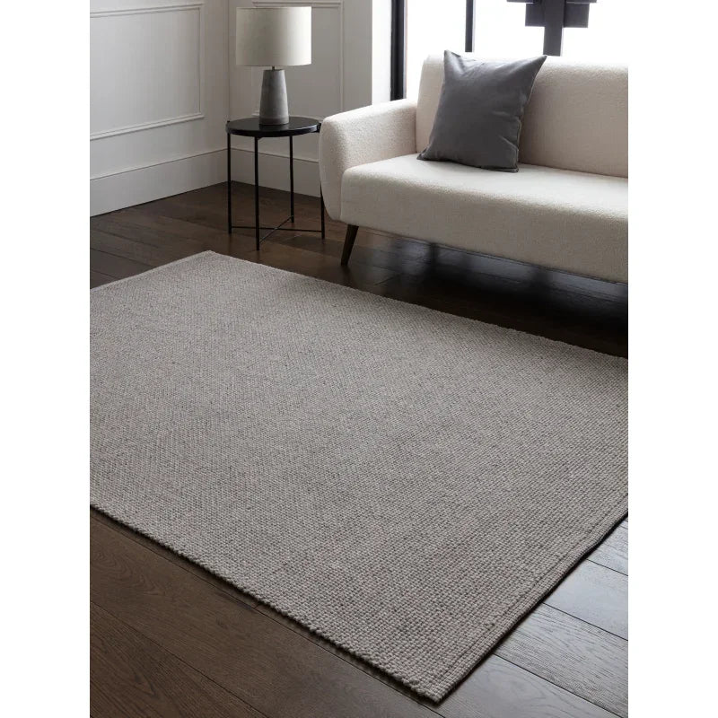 Light grey textured rug on dark wood floor in modern living room with cream sofa and side table