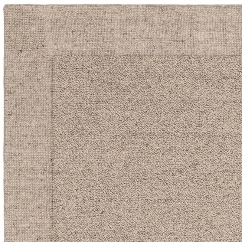 Closeup of taupe textured area rug corner with subtle border detail