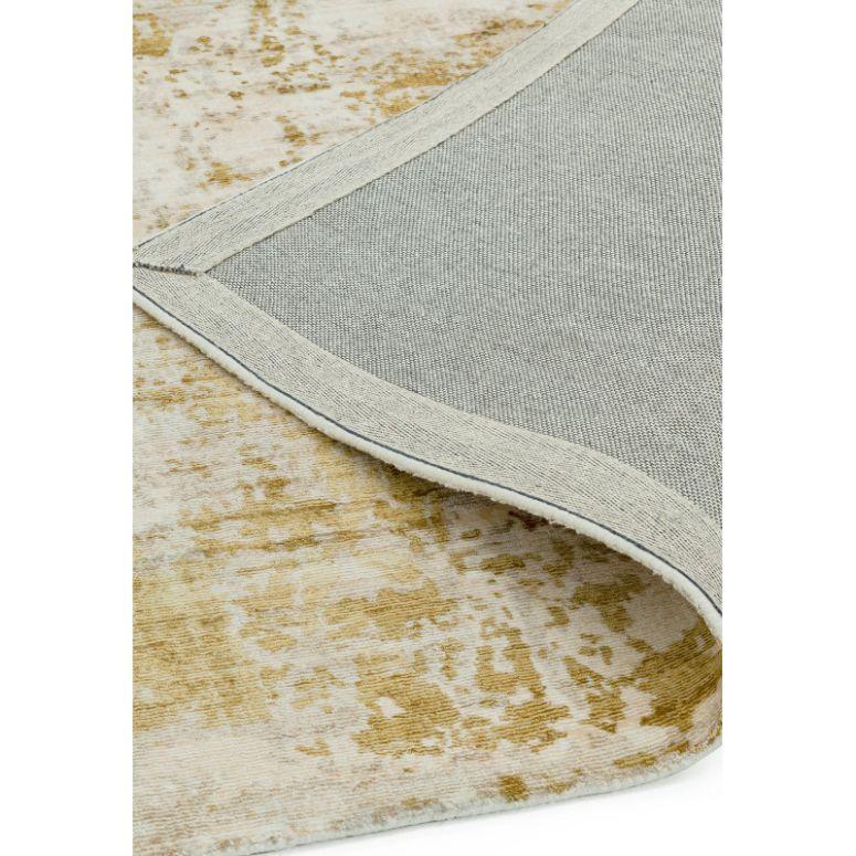 Closeup of abstract patterned area rug in beige and gold, showing woven backing corner
