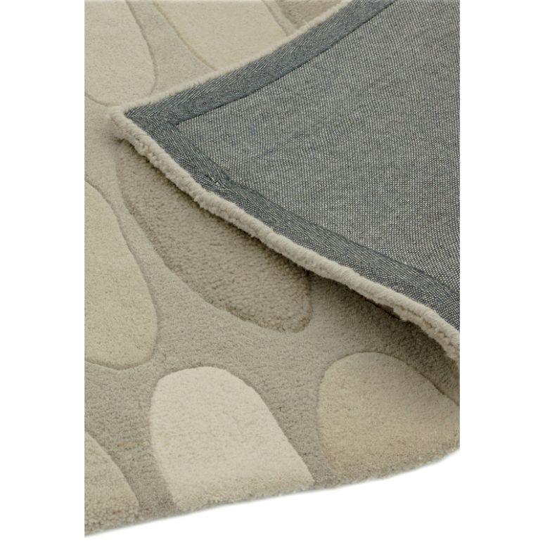 Beige patterned area rug corner with textured pile and grey fabric backing visible