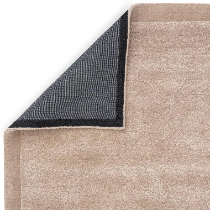 Beige area rug with corner folded to show non-slip black backing