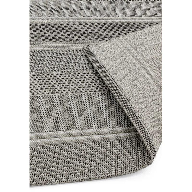Grey woven rug with textured geometric patterns and folded corner detail