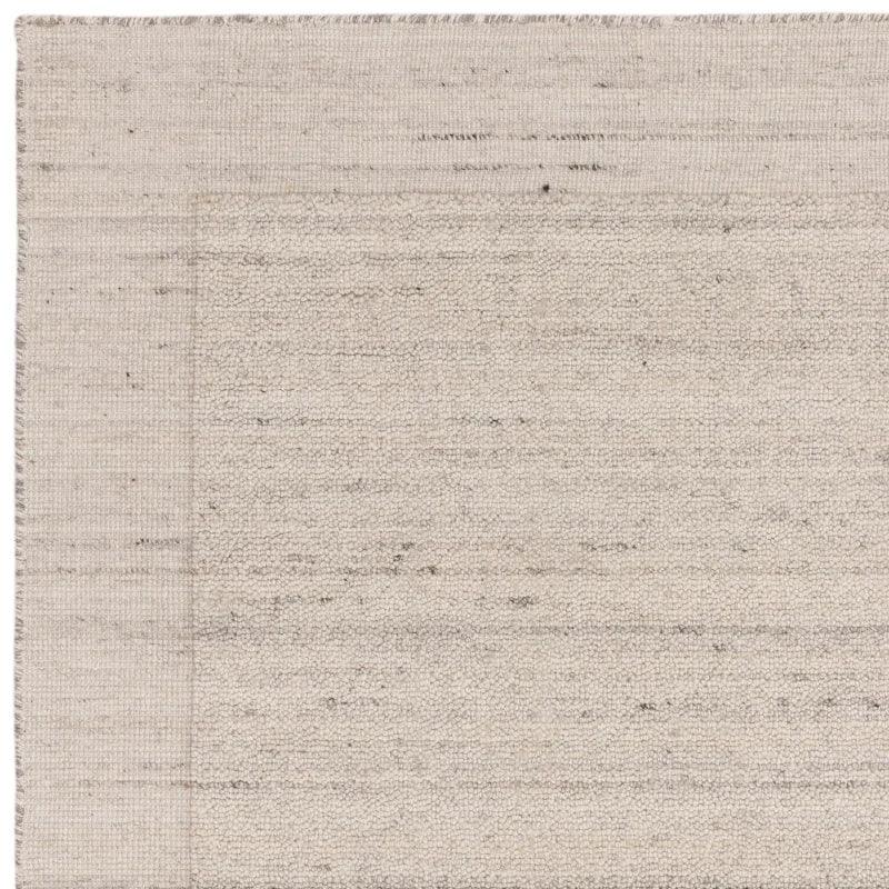 Neutral wool area rug with textured weave and subtle border detail, close-up view
