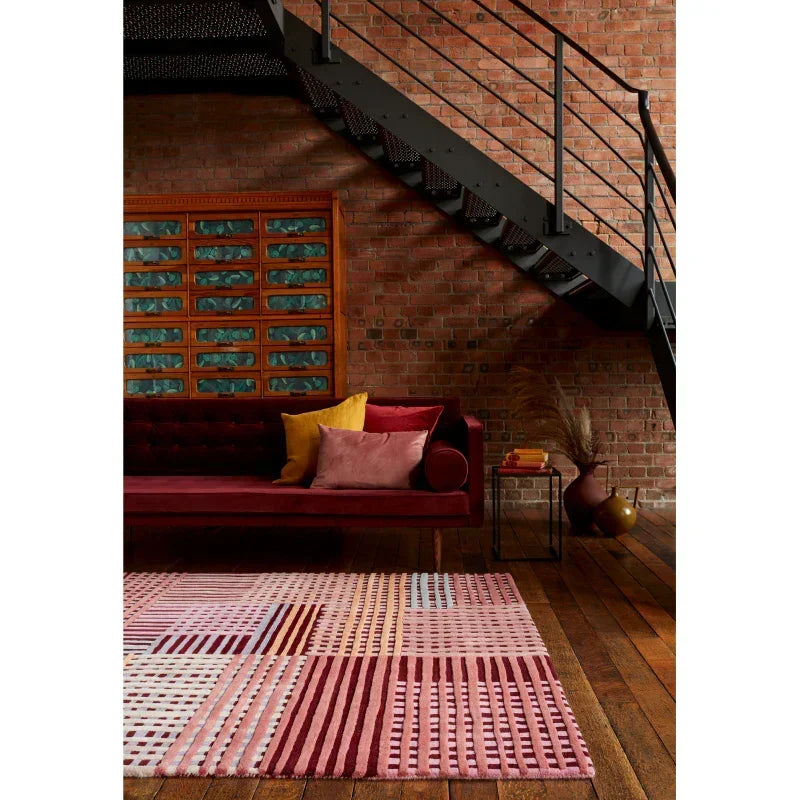 Geometric patterned red and pink rug on wooden floor with velvet sofa in modern loft room