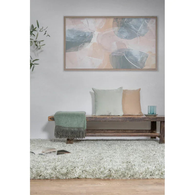 Wooden bench with pastel cushions, throw, and glassware on shaggy white rug in living room