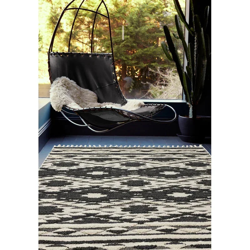 Monochrome patterned area rug on floor with black leather hanging chair and potted cactus