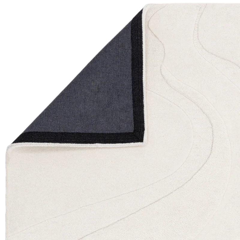 Close-up of cream area rug with textured pattern and black corner backing