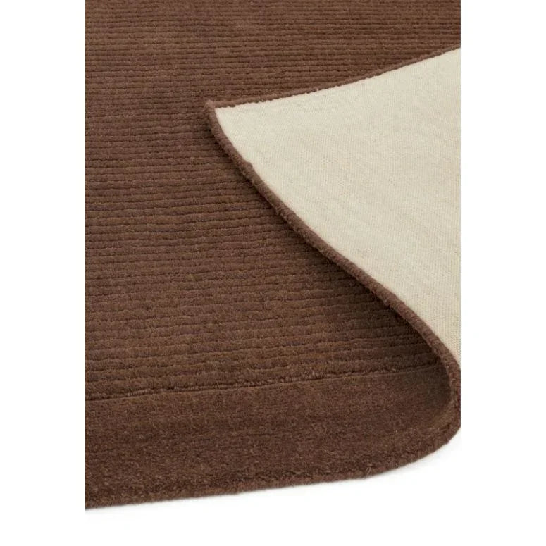 Brown textured area rug with corner flipped to show cream underside and border detail