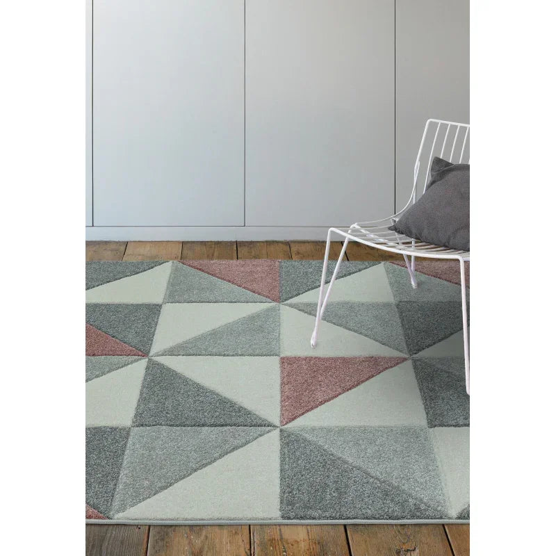 Geometric patterned rug in soft grey and pink tones on wooden floor beside white chair