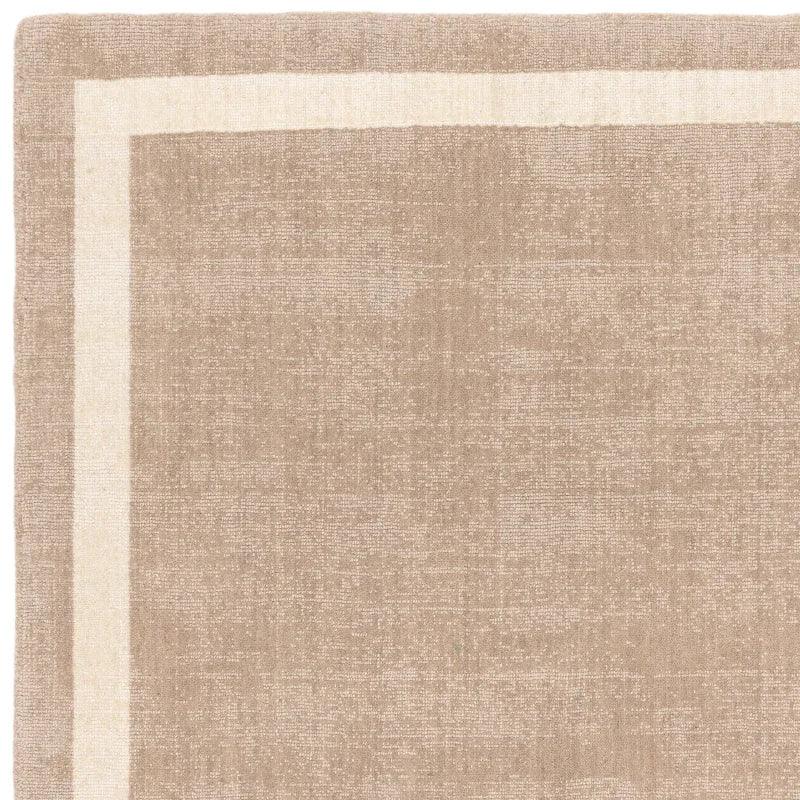 Beige area rug with cream border and subtle woven texture, close up of corner detail