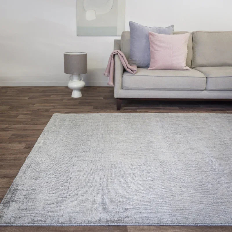 Light grey area rug on wood floor beside beige sofa with pastel cushions