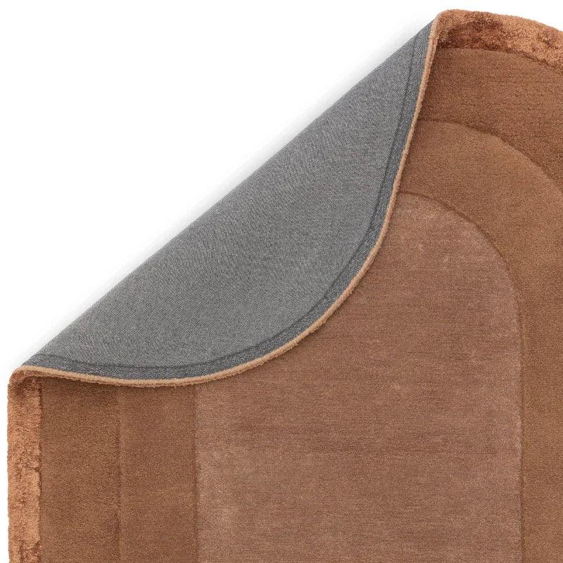Corner of brown area rug with textured border and non-slip grey backing