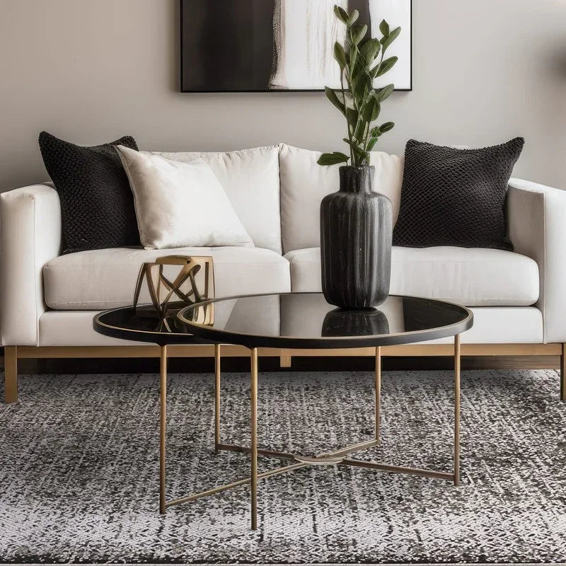 Modern black glass coffee table with gold frame in front of white sofa and monochrome cushions