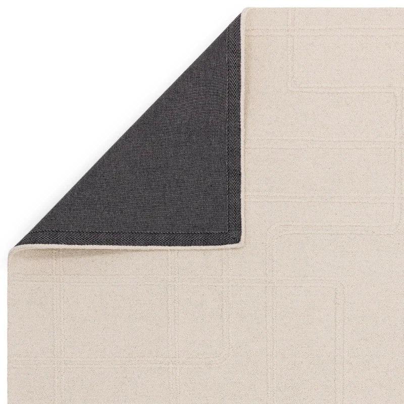 Beige textured rug with geometric pattern and corner flipped showing dark backing