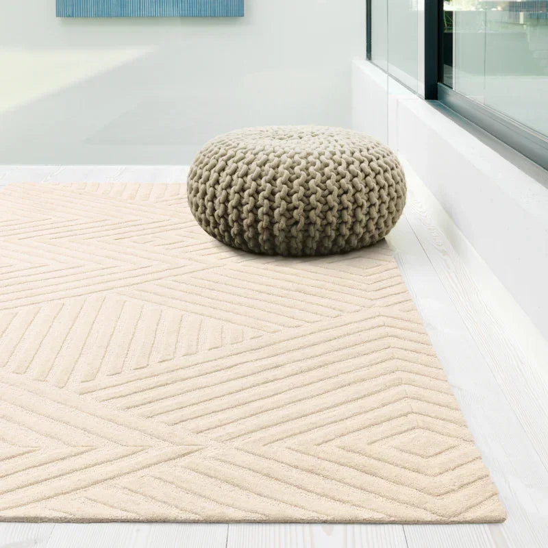 Beige geometric area rug with textured pattern beside chunky knit pouffe in modern living space