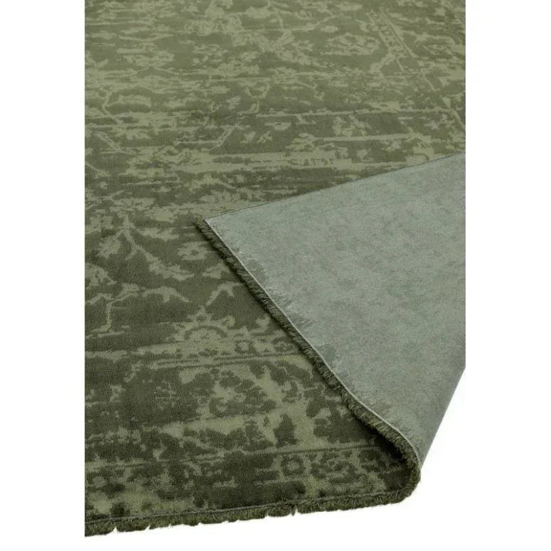 Green patterned rug with detailed border, corner flipped to show backing