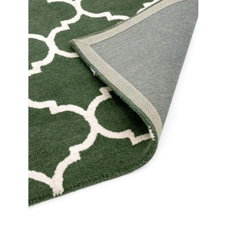 Green patterned rug with white geometric design, corner flipped to show backing