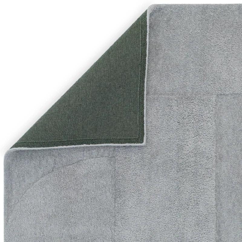 Light grey area rug with textured surface and corner folded to show non-slip backing