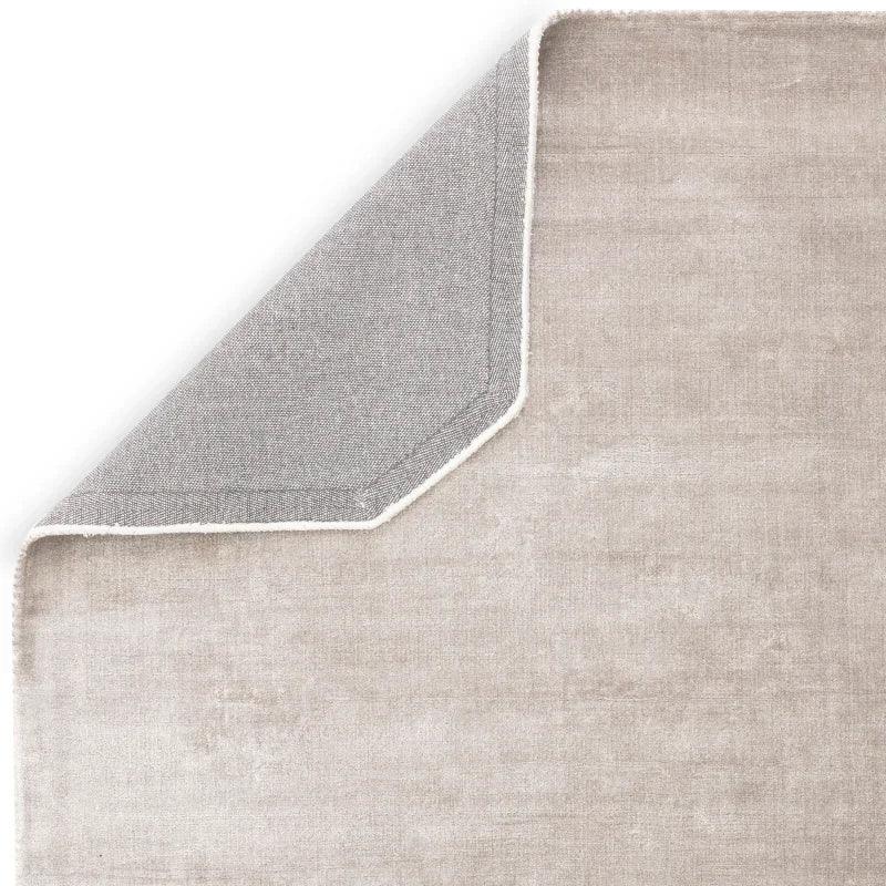 Close-up of beige area rug with corner flipped showing textured backing