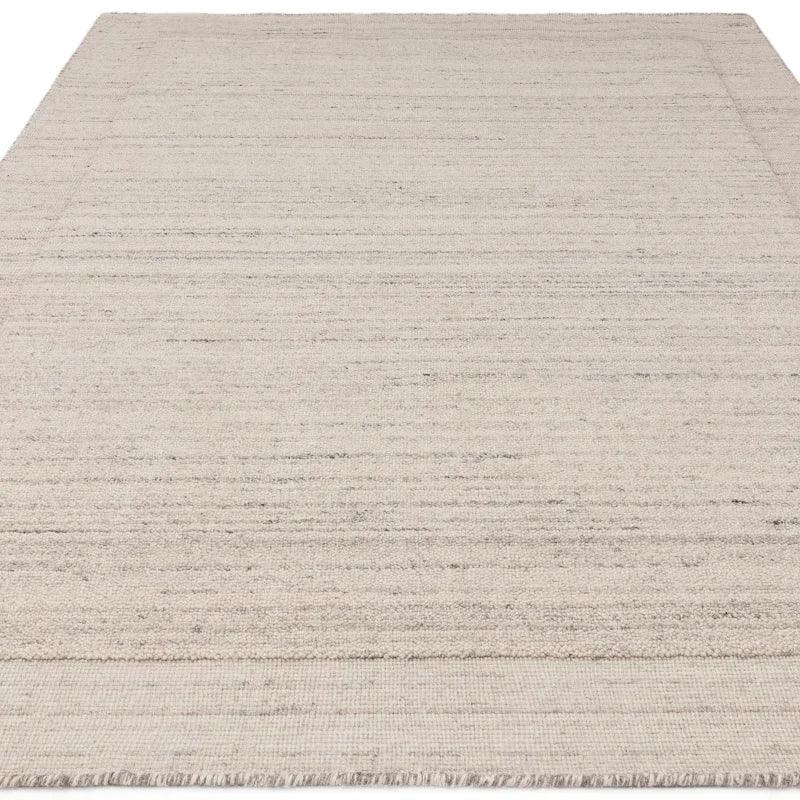 Beige woven area rug with subtle textured pattern and fringed edges on light background