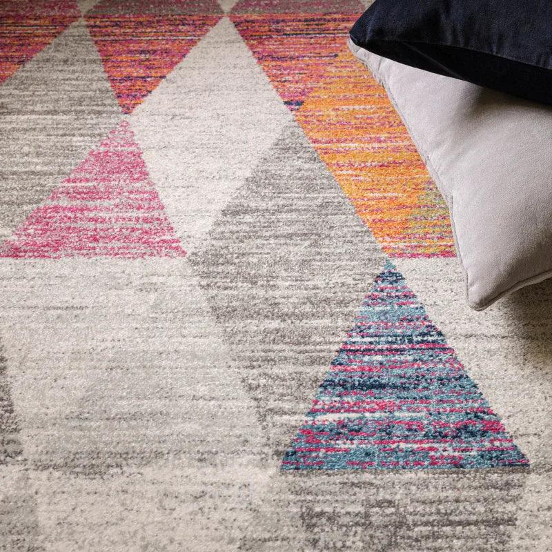 Modern geometric area rug with pink, grey, blue triangles beside two scatter cushions