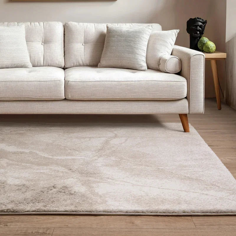 Beige sofa with wooden legs and cushions on marble effect rug in modern living room