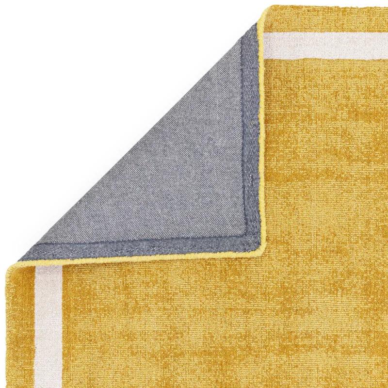 Yellow and white area rug corner folded to show grey fabric backing