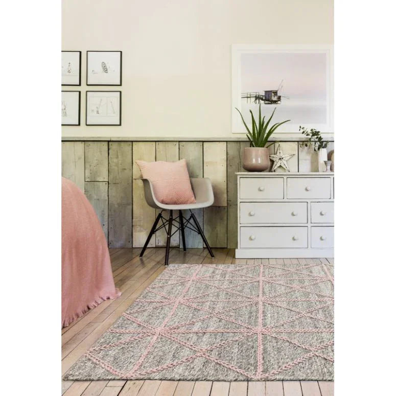Grey and pink geometric rug on wooden floor in cosy bedroom with modern chair and dresser
