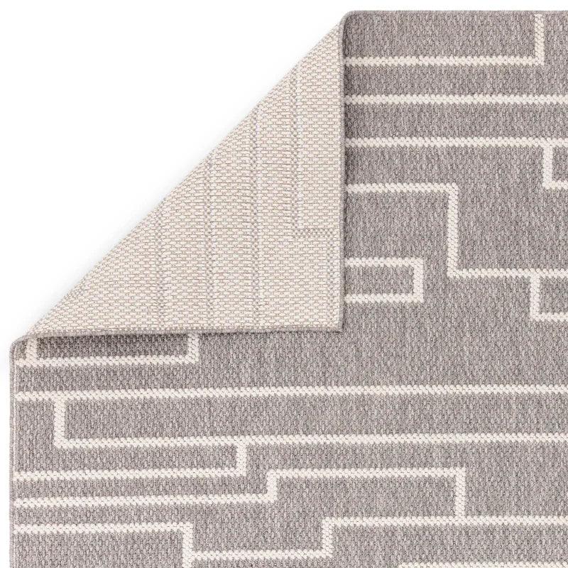 Grey geometric pattern rug with corner flipped to show textured backing