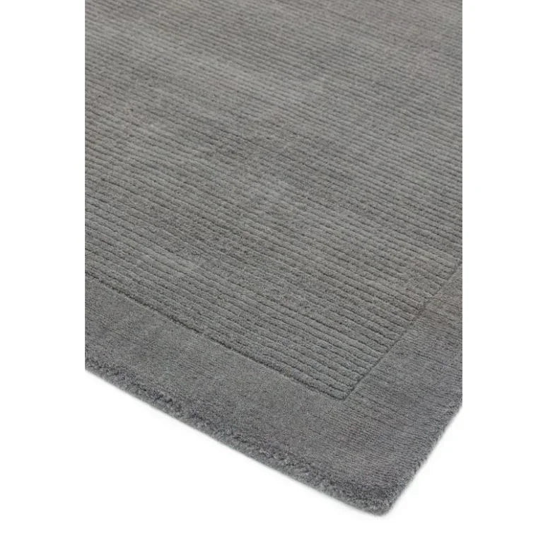 Grey wool rug with subtle textured lines and bordered edge, shown from angled corner view