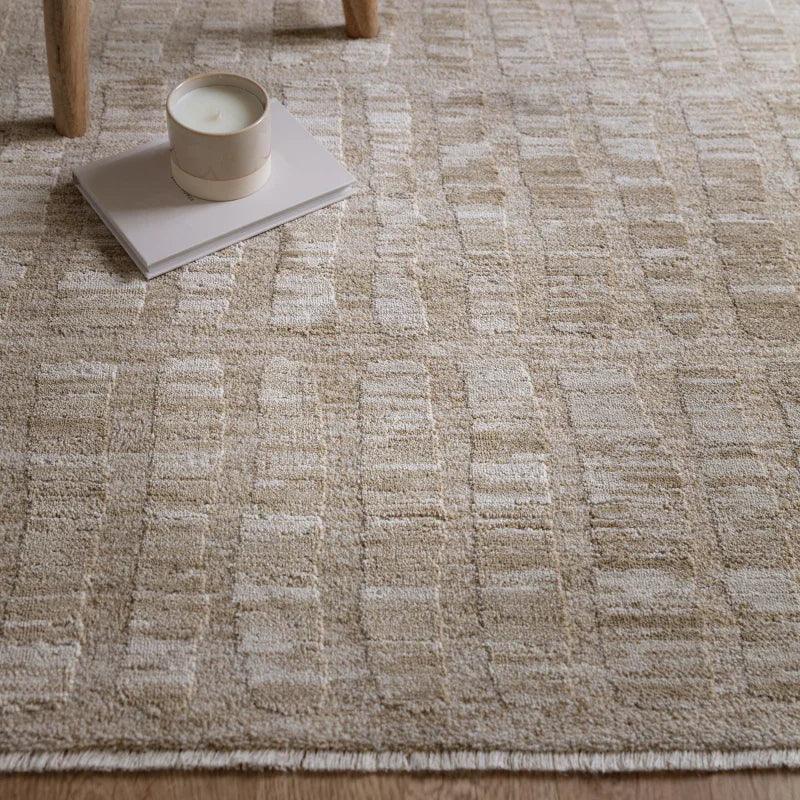 Beige patterned rug on wooden floor with candle and book on top