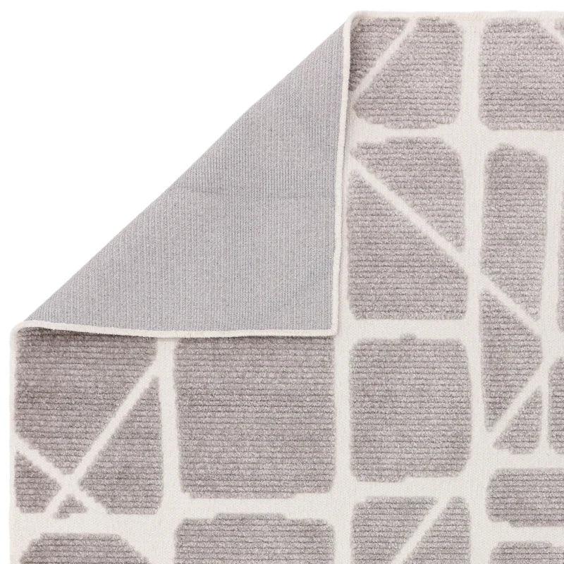 Modern grey geometric area rug with textured pattern and corner flipped to show backing