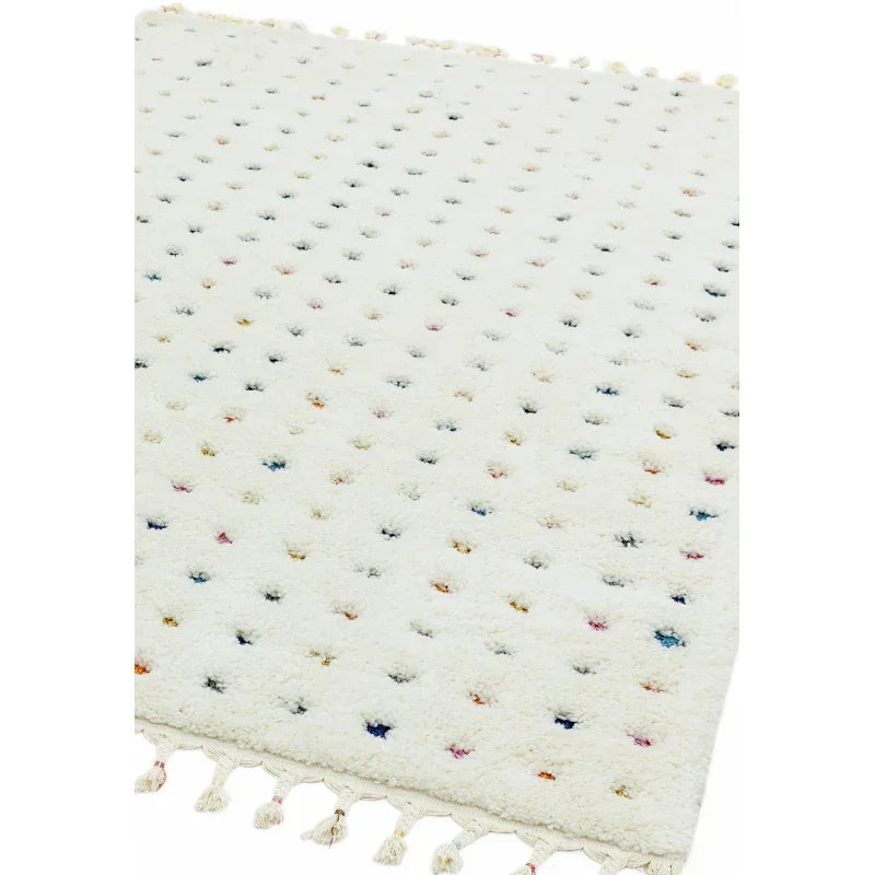 White wool rug with multicolored tufted dots and tassel fringe, angled view