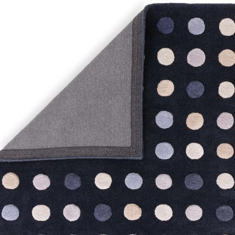 Black polka dot pattern rug with neutral tones, corner flipped to show backing detail
