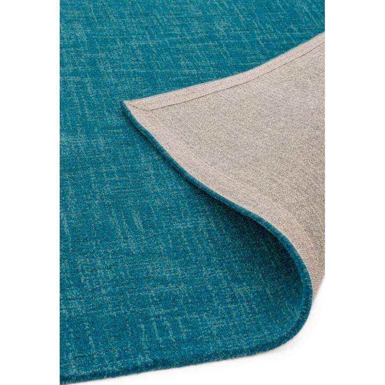 Blue textured area rug with beige backing, shown corner turned up